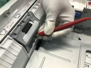 A gloved hand fixes a printer using a red precision tool, showcasing maintenance skills.